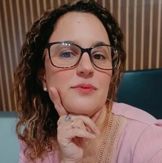 Lindsay Ribeiro de óculos e blusa rosa, com a mão no queixo